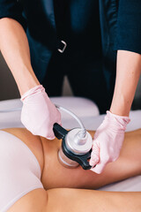 Woman, a beautician doing radiofrequency RF treatment on her client's thigh in a beauty salon.