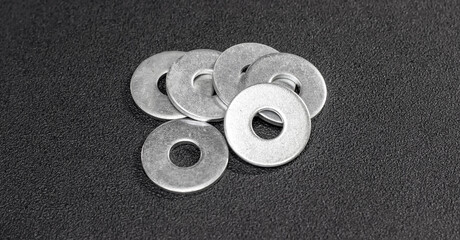 Metal washers neatly arranged on a matte black surface. Metal washers for bolts and screws. The subdued backdrop, emphasizing the precision of the metal washers. - obrazy, fototapety, plakaty