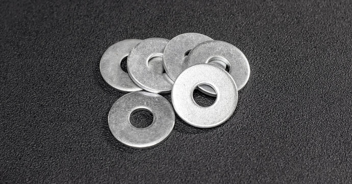 Metal washers neatly arranged on a matte black surface. Metal washers for bolts and screws. The subdued backdrop, emphasizing the precision of the metal washers.