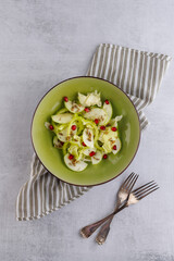 Green salad with fresh vegetables and fruits. Salad of green apple and green peppers with pomegranate seeds in a green plate.
