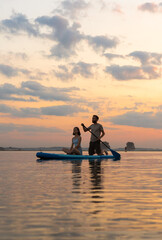 Happy couple paddle boarding at lake during sunset together. Concept of active family tourism and supping. aesthetically wide shot.