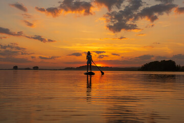 silhouette of woman on inflatable SUP board and paddling through shining water surface. aesthetically wide shot. Freedom happy female at sunset on a lake