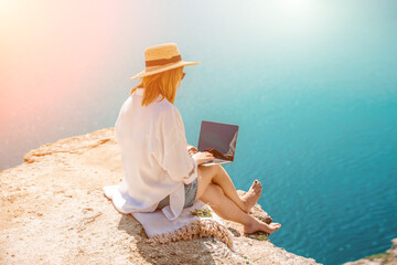 Freelance woman working on a laptop by the sea, typing away on the keyboard while enjoying the...