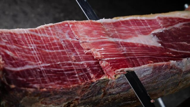Knife cutting slicing a traditional Iberico Spanish ham, jamon. Whole leg. Close up