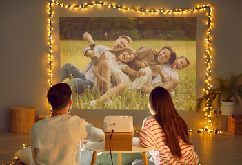 Projection family pictures on wall, using video projector, happy people in love sitting close enjoy...
