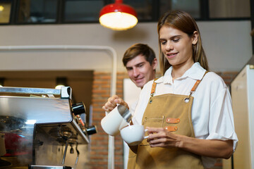 Professional Asian female barista pouring a hot milk over the espresso in coffee cup. Happy female...
