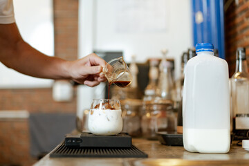 Professional Asian male barista pouring a cold milk in a glass. Happy male barista making a cup of...
