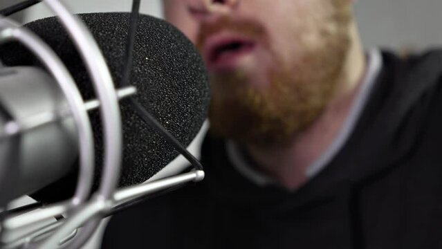 close-up of professional microphone in focus with middle-aged man with red beard conducting radio broadcast in the background. professional podcast recording equipment.
backstage of the radio studio