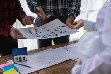 A team of construction workers and engineers meet to plan home construction and plan an office...