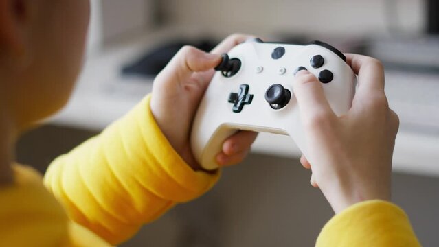 The teenager holds a large white gamepad in his hands and actively presses buttons. Close-up of the hands. Live Hand Held shooting