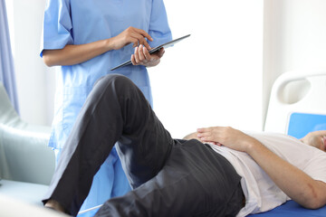 Nurse doing leg and knee physiotherapy to male patient in hospital examination room.
