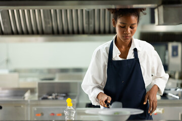 Happy African American woman standing with arms crossed while working as chef in a restaurant....
