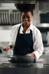 Happy African American woman standing with arms crossed while working as chef in a restaurant. Cooking class. culinary classroom. happy young african woman students cooking in cooking school. - obrazy, fototapety, plakaty