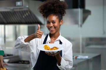 Happy African American woman standing with thump up while working as chef in a restaurant. Cooking...