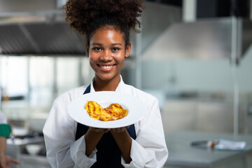 Portrait Happy African American female show omelet while working as chef in a restaurant. Cooking...