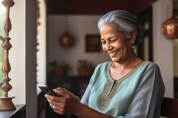 A  senior woman of Indian ethnicity with smiling face having a communication through mobile phone - obrazy, fototapety, plakaty