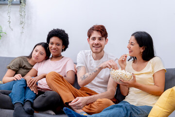 Group of friends sharing popcorn and enjoying leisure time together on a sofa. 