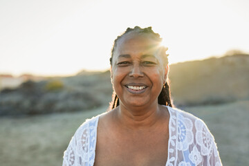 Senior african woman smiling on camera during travel vacation on the beach with sunset in the...