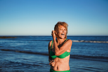 Happy senior latin woman smiling on camera during summer travel vacation on the beach