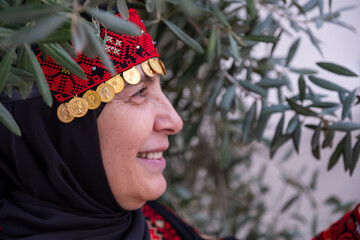 Portrait Of woman wearing palestinian traditional clothes in olive trees field holding branch in...
