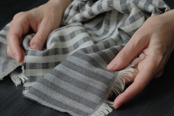 Women's hands unfold a gray scarf on the dark surface of the table. Demonstration of the quality of...