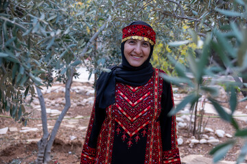 Portrait Of woman wearing palestinian traditional clothes in olive trees field holding branch in...
