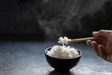 The man hand of using black chopsticks holding hot jasmine rice with smoke and steam in black bowl...