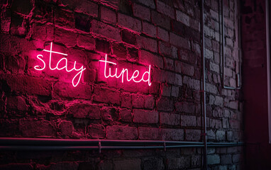 Red neon light text "stay tuned" against brick wall.