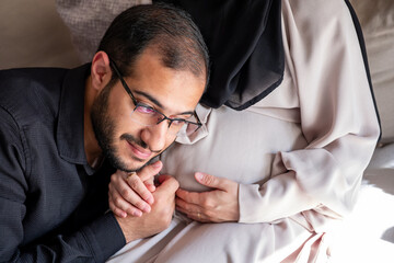 Arabian man is listening to his beautiful pregnant wife's tummy and smiling