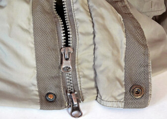 The lock is a zipper with two metal fasteners and rivets on a beautiful light gray jacket for men.