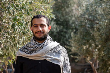 portrait for male wearing keffiyeh in olive tree field with black background and black shirts also with smile facial expression