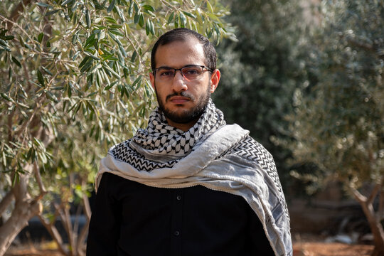 portrait for male wearing keffiyeh in olive tree field with black background and black shirts also with angry facial expression