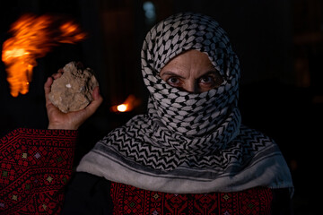 portrait for old woman holding stone which represents the only weapon against the occupation and...