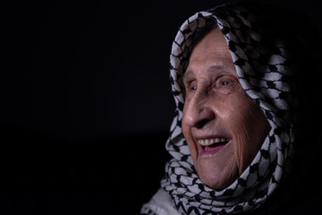 portrait of an old lady in dark background wearing white palestinian keffiyeh with smile on her face looking for freedom and hope to Right of Return for Palestinians