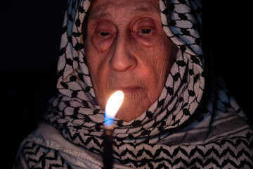 Portrait of old lady wearing white palestinian keffiyeh in dark holding the light to freedom...