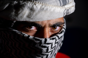 portrait of pearson wearing white keffiyeh on dark background with anger expression on his eyes due...