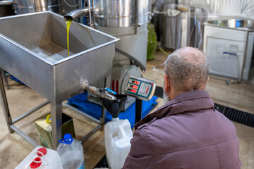 top view for An old Muslim man is engaged in the process of filling fresh olive oil into plastic...