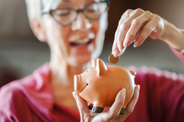 An elderly woman puts a coin into a piggy bank. Savings and banking concept for senior citizens.