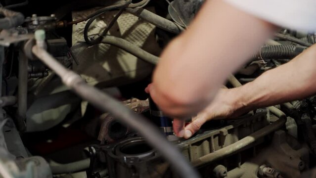 Auto mechanic installs piston using ring compressor tool in engine block for overhaul. Hands work meticulously aligning components for assembly, showcasing detailed car maintenance and repair process.