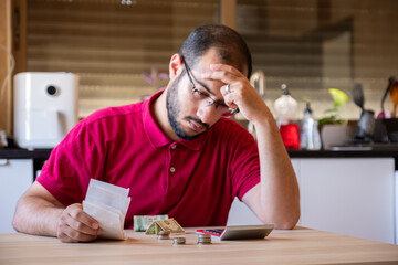 man sitting in the kitchen and calculating the costs of living feeling frustrated - obrazy, fototapety, plakaty