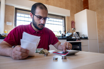 man sitting in the kitchen and calculating the costs of living feeling frustrated