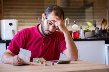 man sitting in the kitchen and calculating the costs of living feeling frustrated