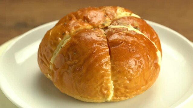 Rotation of homemade cream cheese galic bread in white ceramic plate on wooden table.