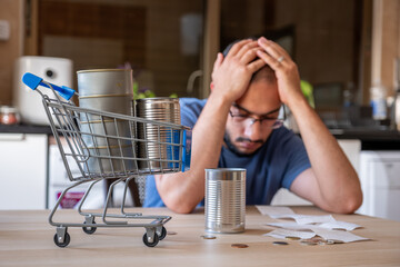 man sitting in the kitchen holding receipt feeling frustrated due inflation and increase of daily...