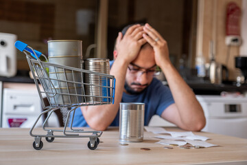 man sitting in the kitchen holding receipt feeling frustrated due inflation and increase of daily...
