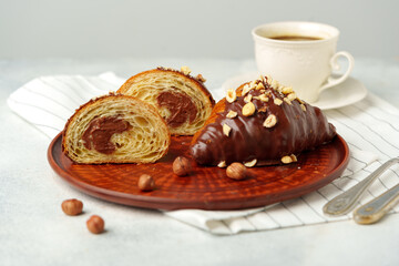 Chocolate croissant on clay plate with cup of coffee on table