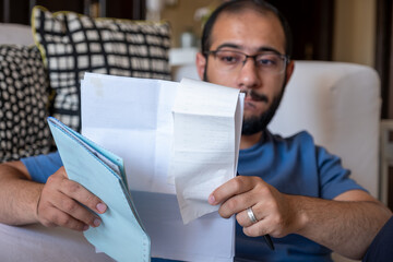 Young Male sitting in the living room checking receipts and using calculator to find the amount of...