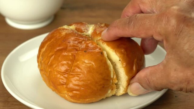 Closeup view of homemade cream cheese garlic bread in white ceramic plate with white ceramic coffee cup on wooden table.