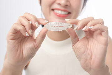 Young smiling woman holding invisalign braces over white background studio, dental healthcare and...