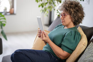Beautiful middle-aged woman using a computer tablet to read a book and surf internet. Modern technologies used by elderly people. Mature woman using digital tablet at home